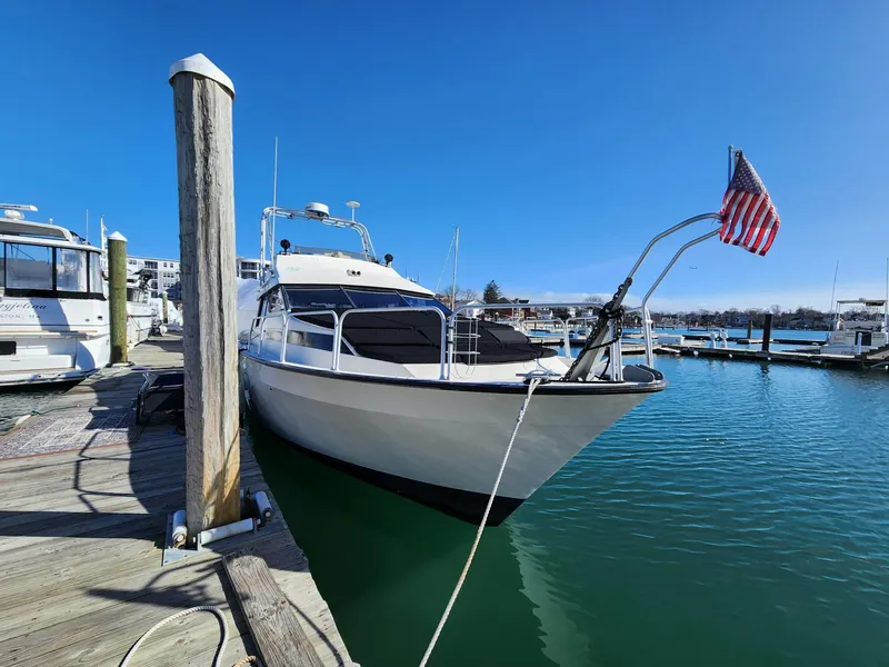 The Image of 1990 Mainship Mediterranean yacht docked at marina with American flag, clear blue sky. - 0