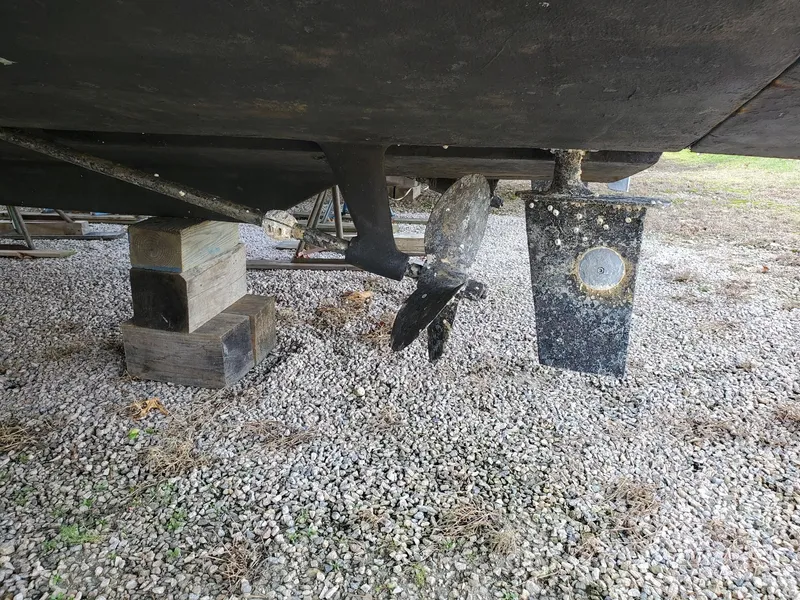 Slide: The Image of 1990 Mainship Mediterranean boat propeller and rudder on gravel, supported by wooden blocks. - 9