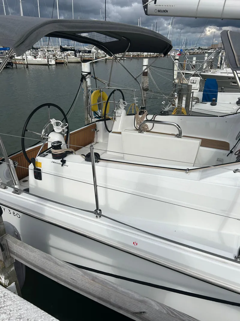 Slide: The Image of 2023 Jeanneau Sun Odyssey 380 sailboat docked at marina, featuring dual steering wheels. - 2