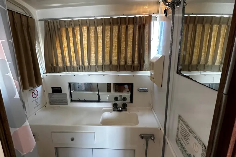 Slide: The Image of 1980 Bertram 33 Sport Fisherman bathroom with sink, mirror, and window with curtains. - 12