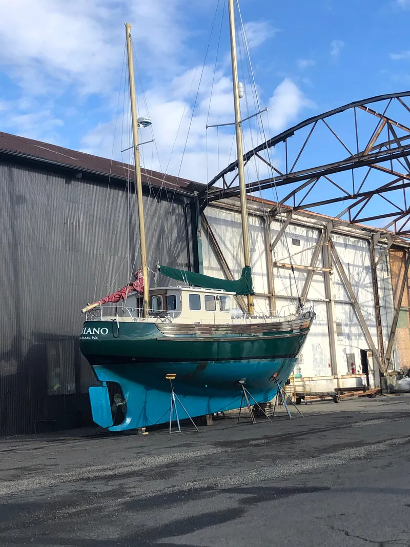 Slide: The Image of 1974 Fisher 37 sailboat on dry dock near industrial building under blue sky. - 6