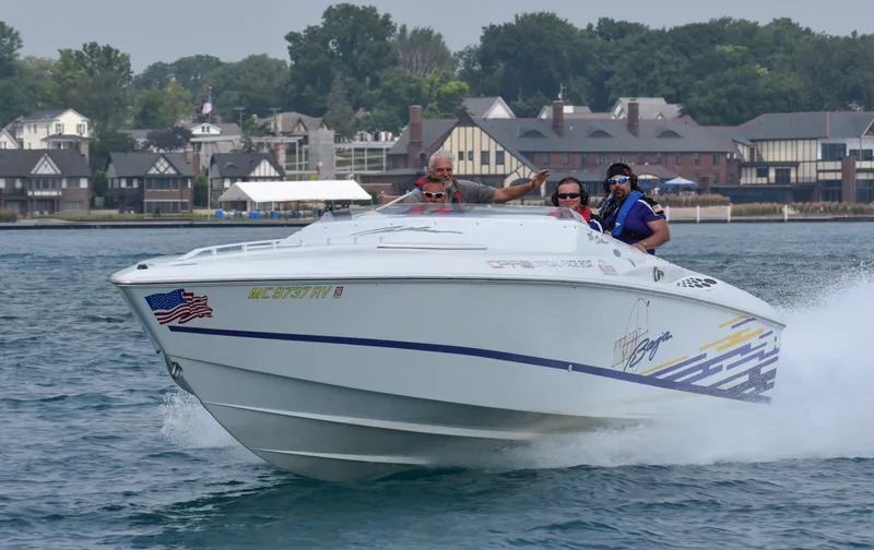 The Image of 1999 Baja 33 Outlaw speedboat cruising on water with three passengers, near a residential shoreline. - 0