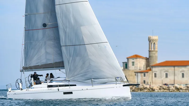 Slide: The Image of 2024 Beneteau First 36 sailboat cruising near a historic coastal building. - 0