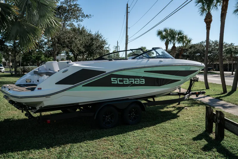 Slide: The Image of 2022 Scarab 255 boat on a trailer, parked on grass with palm trees in the background. - 3