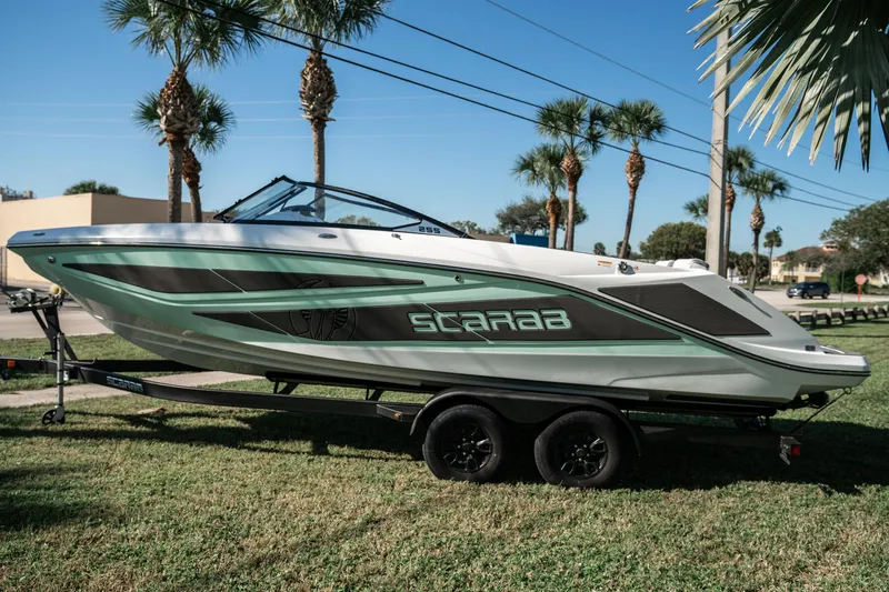 Slide: The Image of 2022 Scarab 255 boat on a trailer, parked on grass with palm trees in the background. - 6
