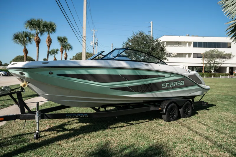 Slide: The Image of 2022 Scarab 255 boat on a trailer, parked on grass with palm trees in the background. - 7