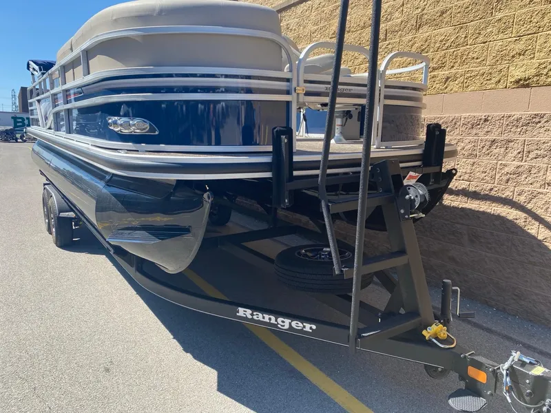 Slide: The Image of 2023 Ranger Reata 220FC pontoon boat on trailer, parked beside a brick wall. - 3