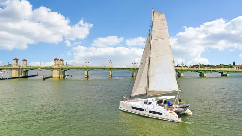 Slide: The Image of Catana 42 sailboat cruising near a scenic bridge under a partly cloudy sky. - 4