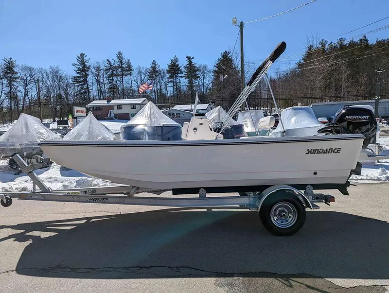 Slide: The Image of 2023 Sundance DX20 boat on trailer in outdoor lot with trees in background. - 11