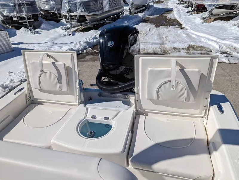 Slide: The Image of 2023 Sundance DX20 boat with open storage compartments and outboard motor in snowy marina. - 7