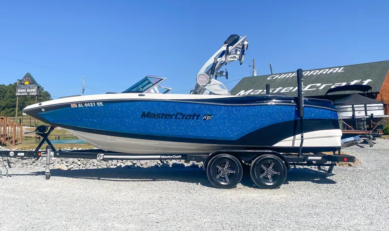 The Image of 2021 MasterCraft XT22 boat on trailer, blue and white design, parked outdoors. - 0
