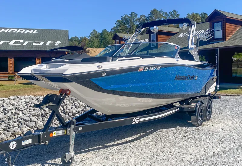 Slide: The Image of 2021 MasterCraft XT22 boat on trailer, blue and white, parked outdoors. - 2