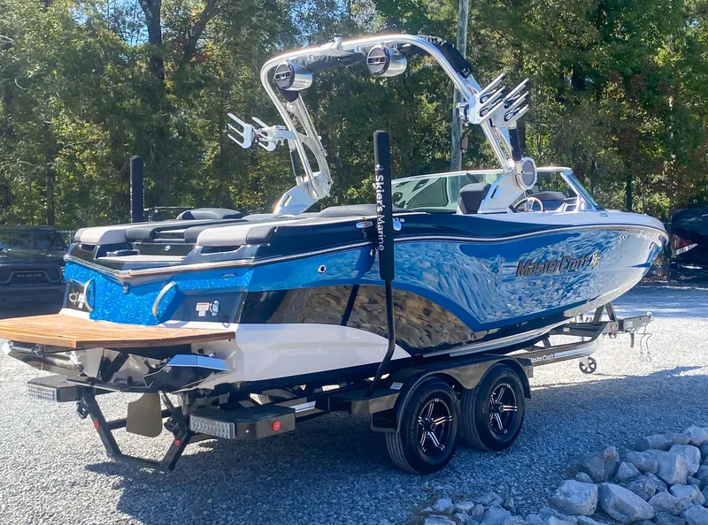 Slide: The Image of 2021 MasterCraft XT22 boat on trailer, blue and black design, parked outdoors. - 6