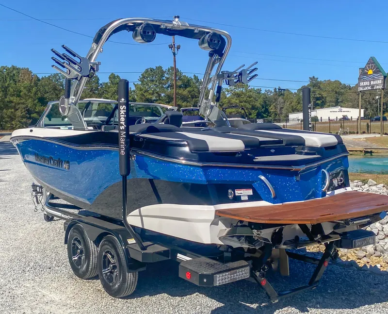 Slide: The Image of 2021 MasterCraft XT22 boat on trailer, blue and white, parked outdoors. - 7