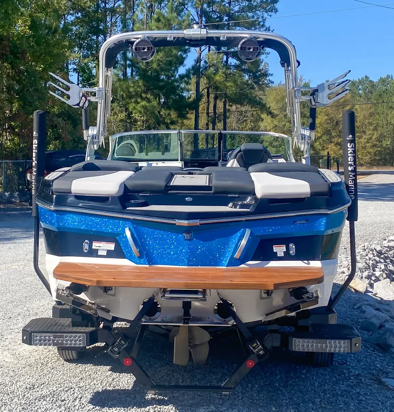 Slide: The Image of 2021 MasterCraft XT22 boat, blue and white, parked on gravel with trees in background. - 8