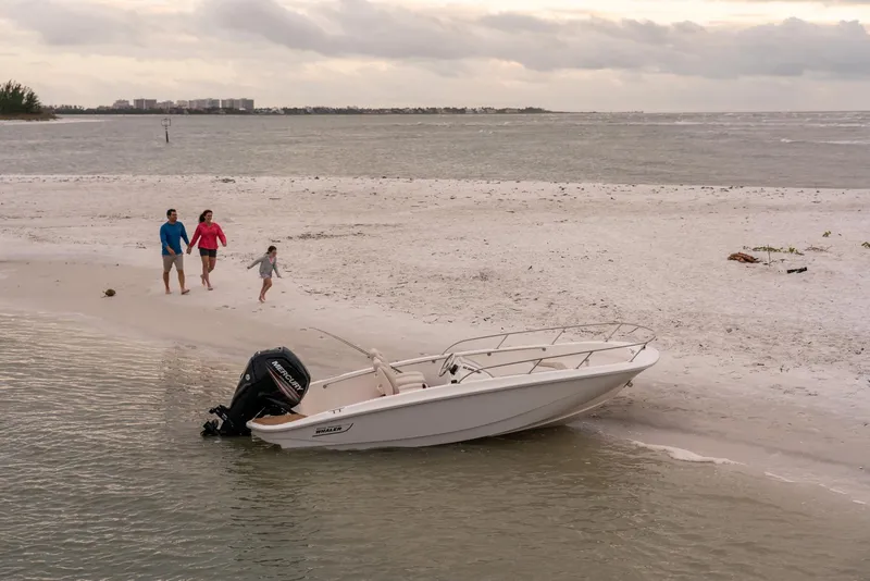 Slide: The Image of 2024 Boston Whaler 160 Super Sport on sandy beach with family walking nearby. - 13