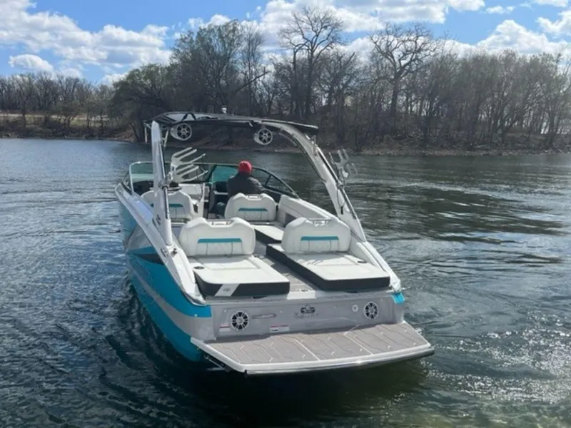Slide: The Image of 2023 Regal LS6 Surf boat on a calm lake with trees in the background. - 19