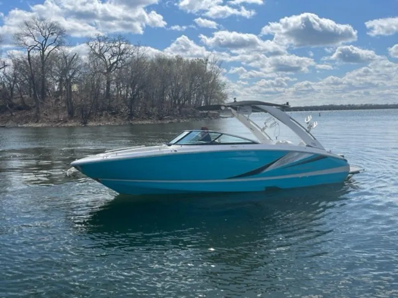Slide: The Image of 2023 Regal LS6 Surf boat on a calm lake under a cloudy sky. - 2