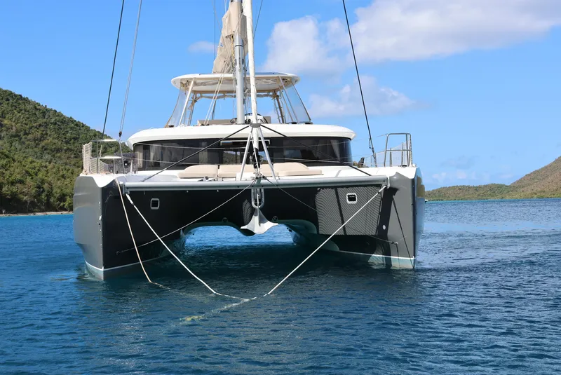 Slide: The Image of 2022 Lagoon 46 catamaran sailing in clear blue waters, surrounded by lush green hills. - 2