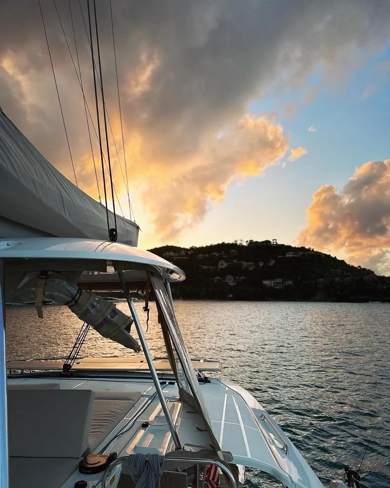 Slide: The Image of 2022 Lagoon 46 catamaran sailing at sunset near a scenic coastline. - 24