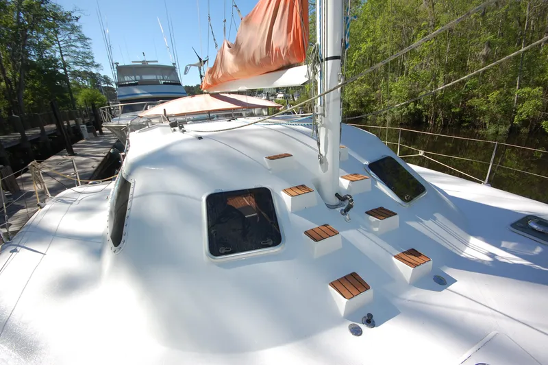 Slide: The Image of 1999 Wildcat 35 Catamaran with orange sail docked near trees. - 12
