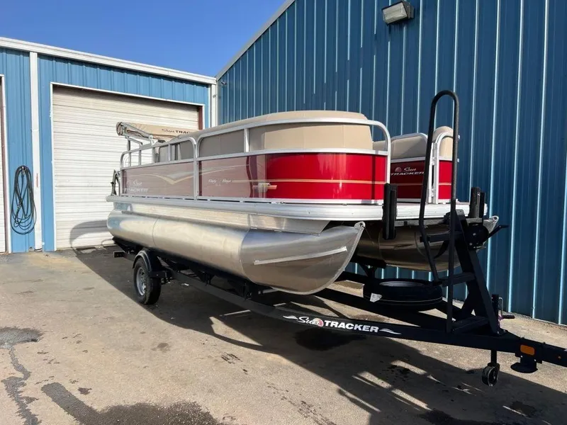Slide: The Image of 2023 Sun Tracker PARTY BARGE® 18 DLX pontoon boat on a trailer outside a blue building. - 7