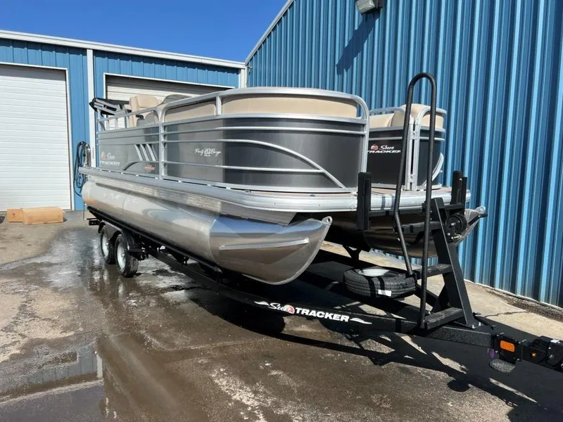 Slide: The Image of 2023 Sun Tracker PARTY BARGE® 20 DLX pontoon boat on a trailer outside a blue building. - 2