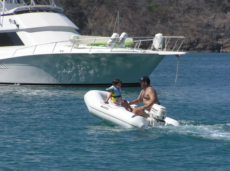 The Image of Man and child on Apex A 10 Lite inflatable boat, 2022, near a yacht. - 1