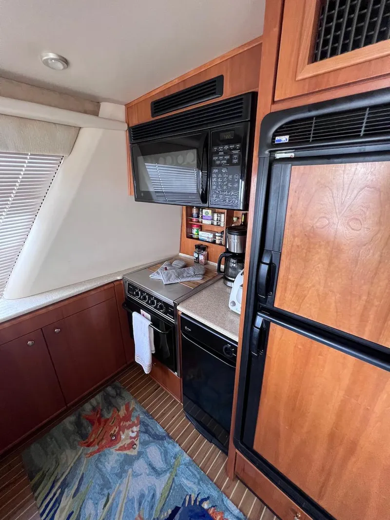 Slide: The Image of 2004 Meridian 490 Pilothouse kitchen with wood cabinetry, appliances, and nautical-themed rug. - 33