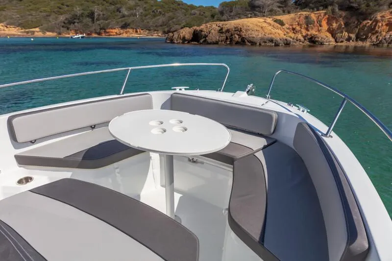 Slide: The Image of 2023 Jeanneau Leader 6.5 CC S3 boat with seating area and table, anchored in clear waters. - 4