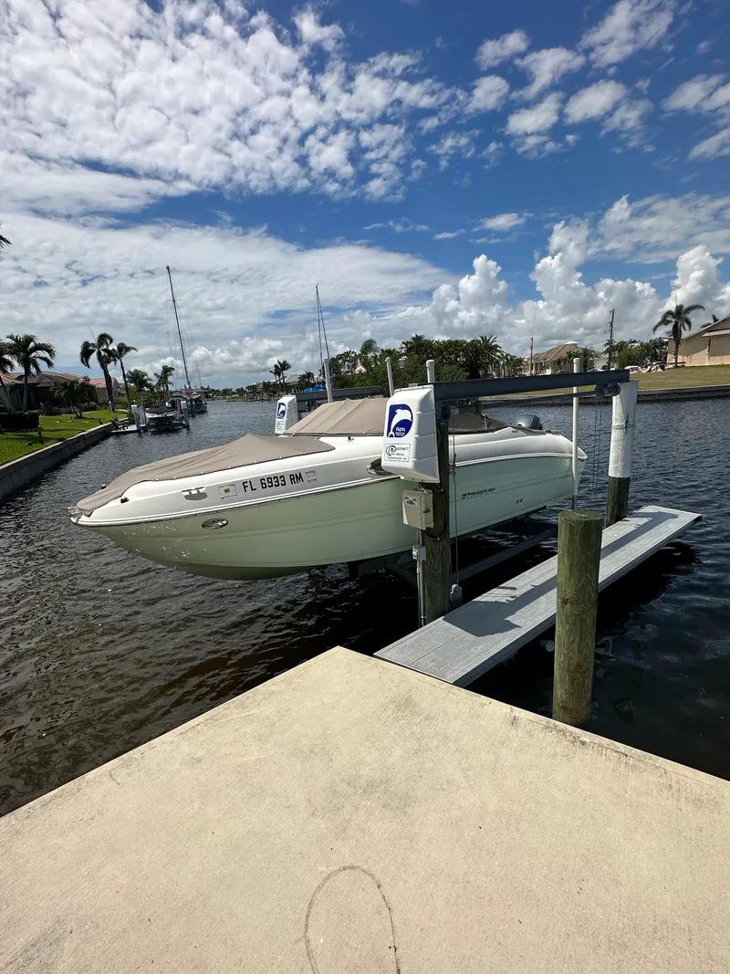 Slide: The Image of 2018 Stingray 214 LR boat docked on a lift in a sunny canal setting. - 2