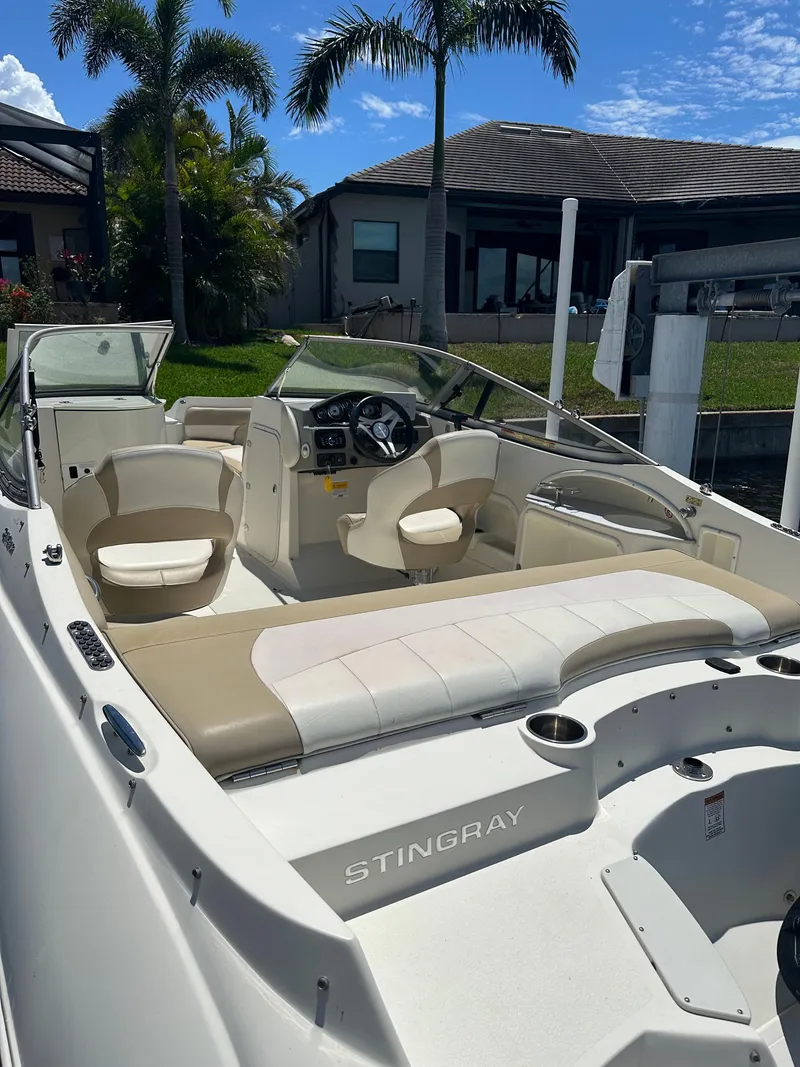 Slide: The Image of 2018 Stingray 214 LR boat with beige seating, docked near a house and palm trees. - 5
