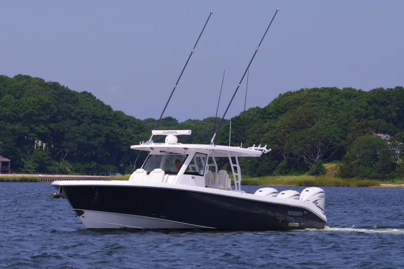 Slide: The Image of 2024 Everglades 395 Center Console boat cruising on a lake with lush green shoreline. - 4