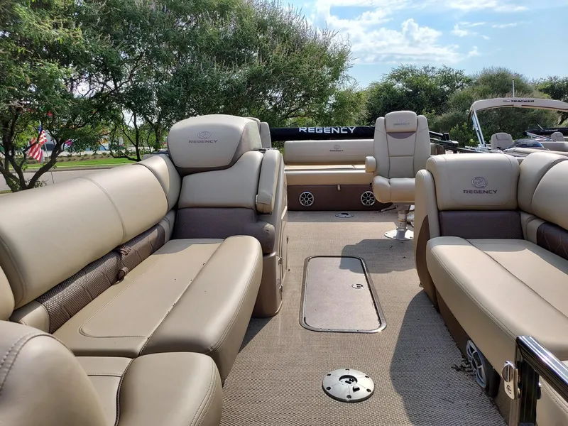 Slide: The Image of 2023 Regency 230 LE3 Sport boat interior with beige seating and lush greenery in the background. - 3