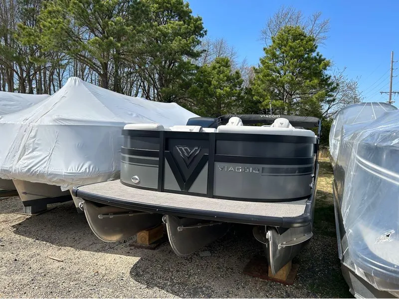 The Image of 2023 Viaggio D23U pontoon boat in storage, surrounded by trees and covered boats. - 1