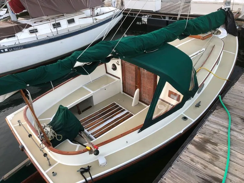 Slide: The Image of 1977 Marshall 22 sailboat docked, featuring green canvas covers and wooden accents. - 11