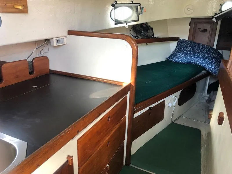 Slide: The Image of 1977 Marshall 22 boat interior with wooden cabinetry, green bedding, and compact kitchen area. - 8