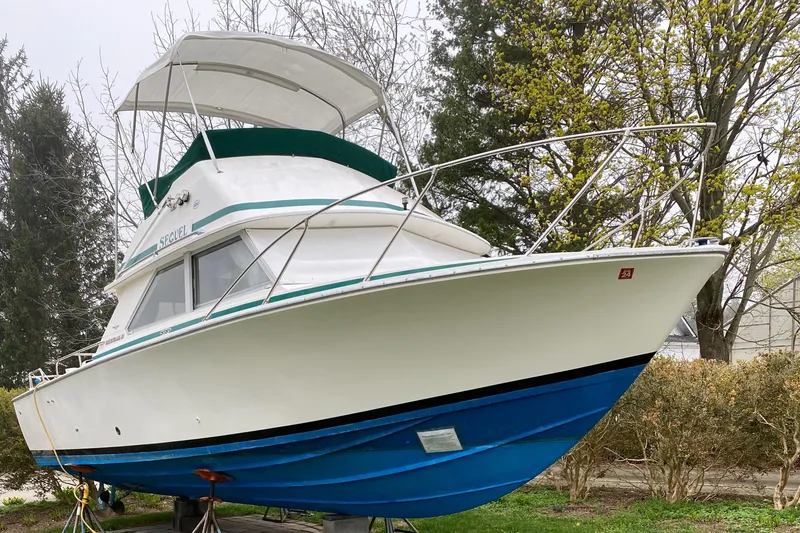 Slide: The Image of 1975 Bertram 28 Flybridge boat on land, white hull with blue bottom. - 21