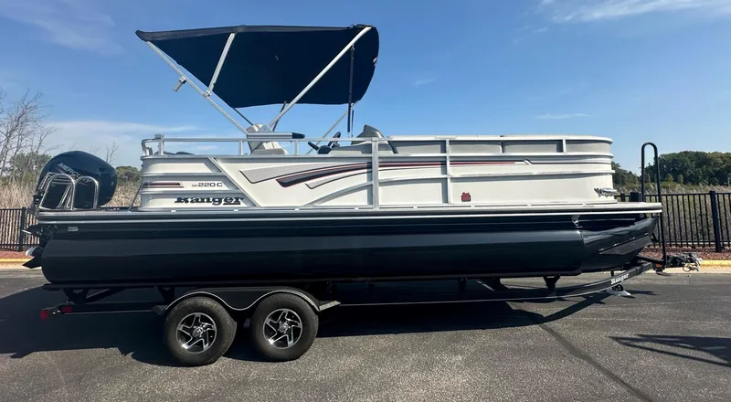 The Image of 2023 Ranger Reata 220C pontoon boat on trailer with canopy, parked outdoors. - 0