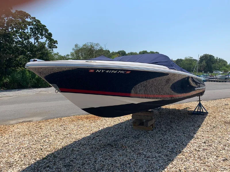 Slide: The Image of 2006 Chris-Craft Launch 25 boat on gravel, covered and elevated, with trees in the background. - 11