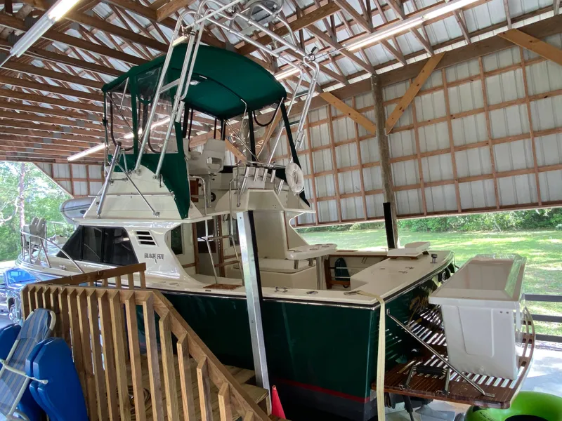 Slide: The Image of 1988 Blackfin 29 Flybridge boat in covered storage, featuring green canopy and wooden deck. - 9