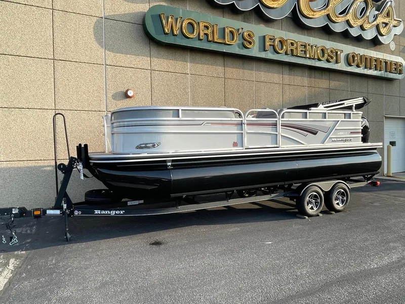 Slide: The Image of 2023 Ranger Reata 220C pontoon boat on trailer outside store. - 1