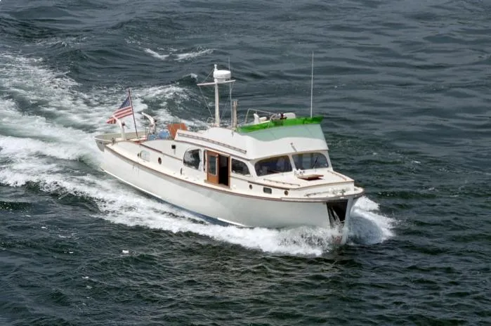 The Image of 1946 Monk Flybridge Sedan boat on calm water with forested shoreline background. - 0