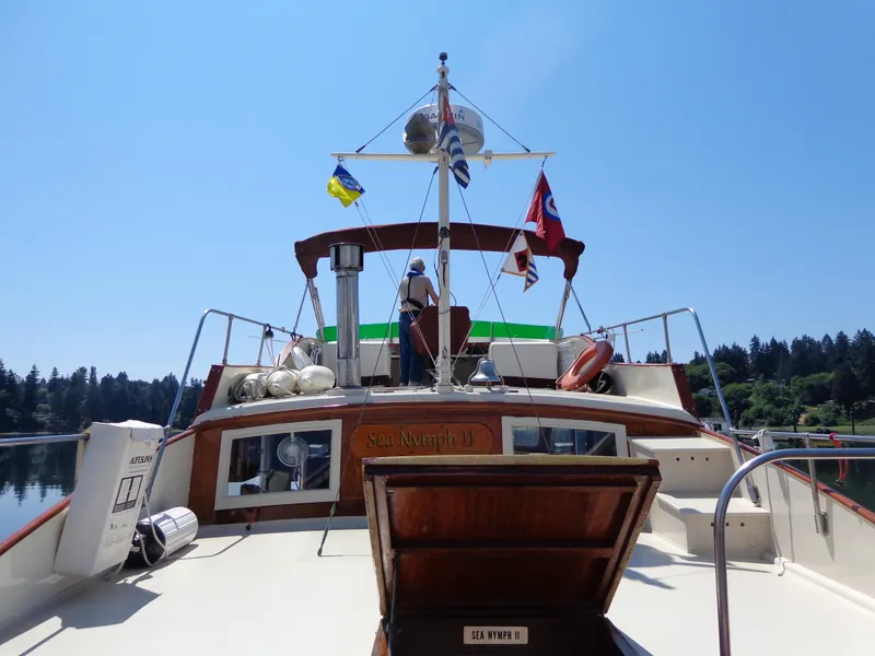 Slide: The Image of 1946 Monk Flybridge Sedan boat on a sunny day, docked near a forested shoreline. - 28