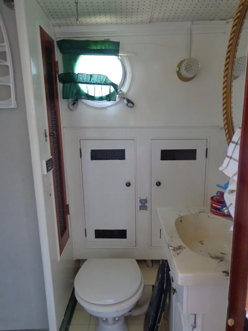 Slide: The Image of 1946 Monk Flybridge Sedan boat bathroom with porthole window, toilet, and storage cabinets. - 31