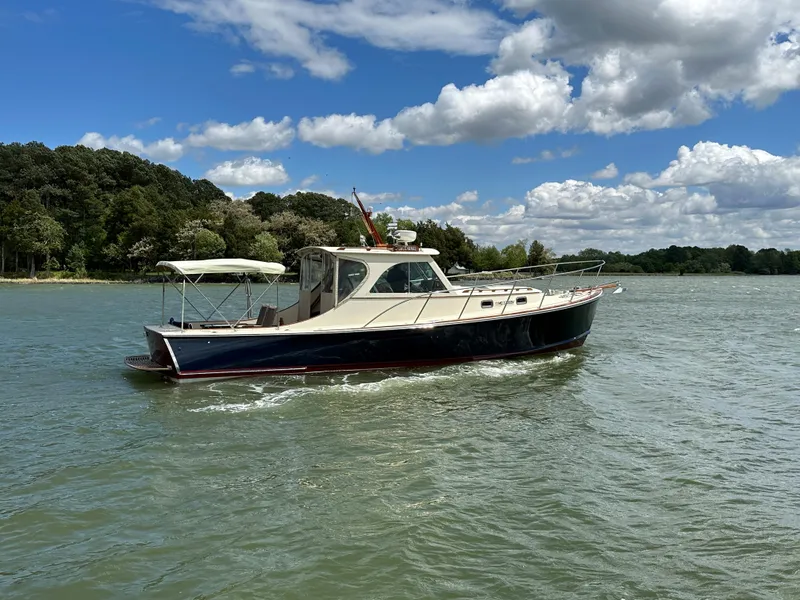 Slide: The Image of 2001 Mast & Mallet 38 Picnic Boat cruising on a scenic lake under a partly cloudy sky. - 24