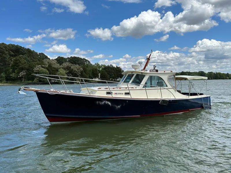 Slide: The Image of 2001 Mast & Mallet 38 Picnic Boat cruising on a scenic lake under a partly cloudy sky. - 6