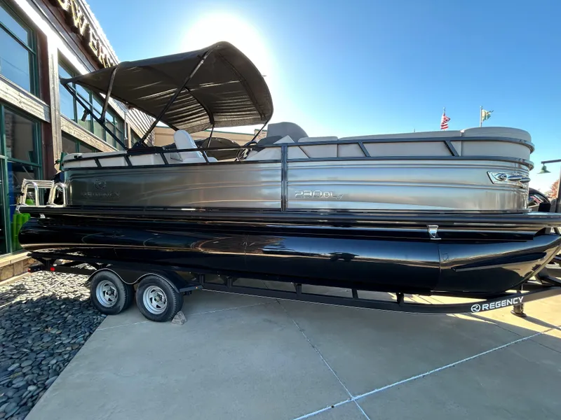Slide: The Image of 2023 Regency 230 DL3 pontoon boat on a trailer, displayed outdoors. - 0
