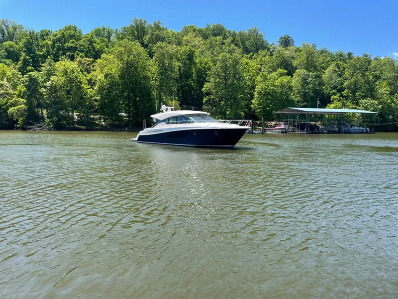 Slide: The Image of 2019 Tiara Yachts C53 cruising on a serene lake with lush green trees. - 2