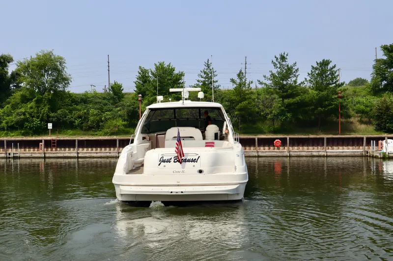 Slide: The Image of 2001 Sea Ray 460 Sundancer yacht docked, rear view with American flag, lush greenery background. - 2